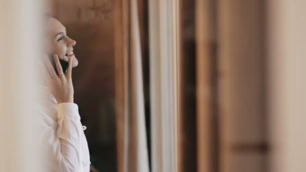 Giovane donna parla al telefono vicino alla finestra — Video Stock