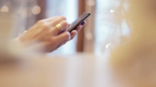 Las manos de la mujer mensajes de texto, utilizando el teléfono inteligente en la cafetería . — Vídeo de stock