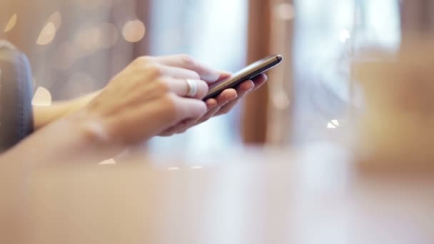 Las manos de la mujer mensajes de texto, utilizando el teléfono inteligente en la cafetería . — Vídeos de Stock