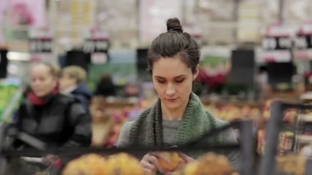 Jeune femme choisit des oranges mûres sur les étagères du magasin . — Video