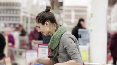 Genç kadın kış şapka süpermarkette seçer.