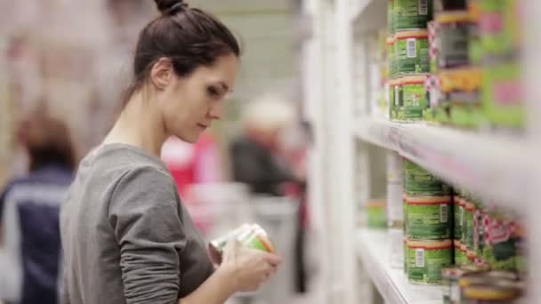 Mujer joven elige comida enlatada en la tienda — Vídeo de stock