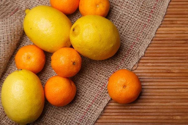 Verse gele citroenen met oranje mandarijnen op zak en bamboe achtergrond close-up — Stockfoto