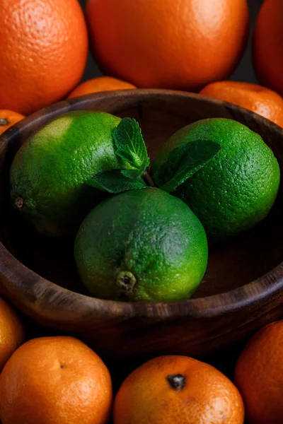 Limes in houten plaat met mandarijnen en munt blaadjes op donkere achtergrond close-up macro — Stockfoto