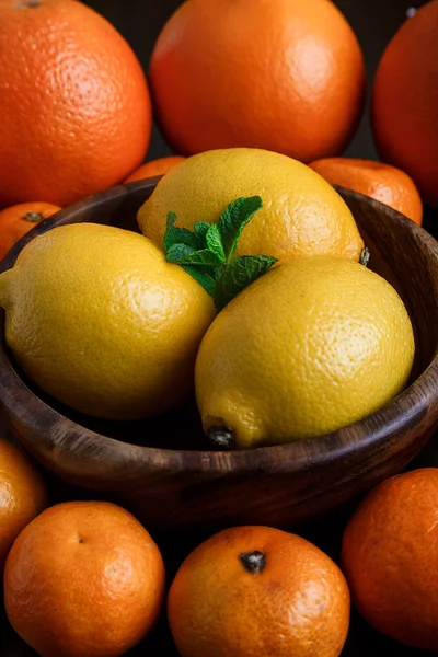 Limoni in piatto di legno con mandarini, arance e foglie di menta su fondo scuro macro primo piano — Foto Stock