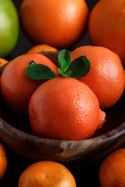 Mandarijnen in houten plaat met mandarijnen, sinaasappels en munt blaadjes op donkere achtergrond close-up macro — Stockfoto