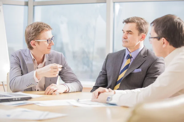 Tres alegres sonrientes jóvenes empresarios o hombres de negocios y clientes que trabajan en offic — Foto de Stock