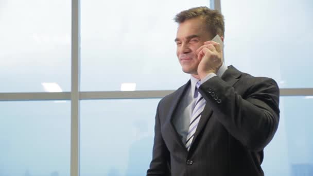 Joyful businessman talking on the phone in bright office against window — Stock Video