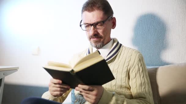 Um homem adulto com uma barba vestida de óculos lendo um livro — Vídeo de Stock