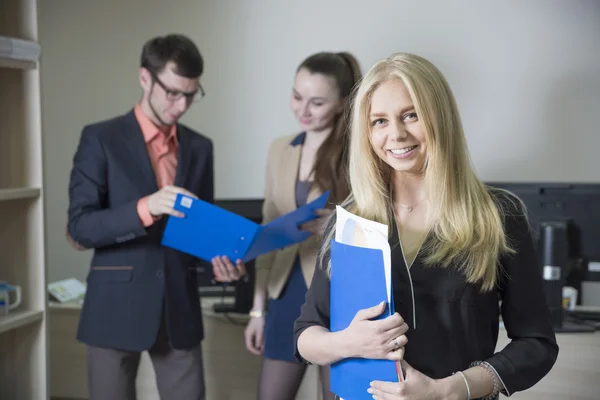 Uma menina estudante sorrindo no fundo de jovens empresários no escritório — Fotografia de Stock