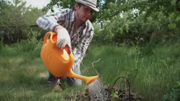 Молодий чоловік в саду поливає рослини з балончика — стокове відео
