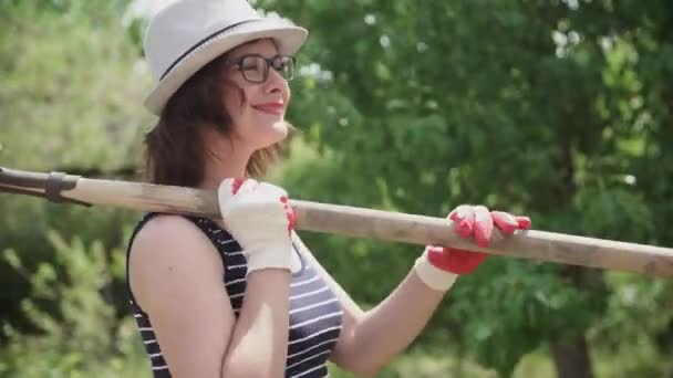 Joven agricultora sosteniendo una pala y sonriendo en el jardín — Vídeos de Stock