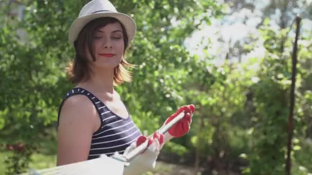 Ung kvinna bonden hålla en kratta och leende i trädgården — Stockvideo