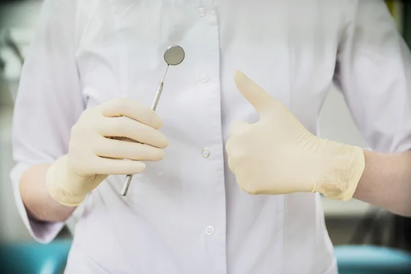 dentist wearing rubber gloves and white holding mouth mirror in hospital