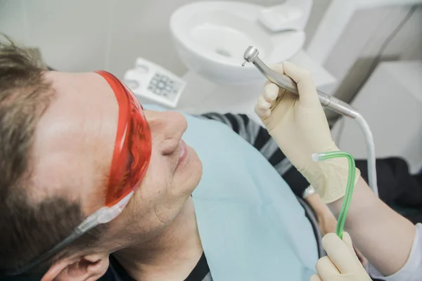 Primer plano concepto de cuidado dental inspección estomatológica. el paciente se acuesta en una silla en odontología delante de él una mano con taladro — Foto de Stock