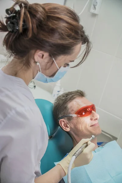 Concepto de cuidado dental inspección estomatológica. el paciente se acuesta en una silla en odontología delante de él una mano con taladro — Foto de Stock