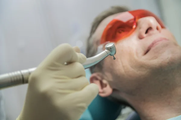 Primer plano concepto de cuidado dental inspección estomatológica. el paciente se acuesta en una silla en odontología delante de él una mano con taladro — Foto de Stock