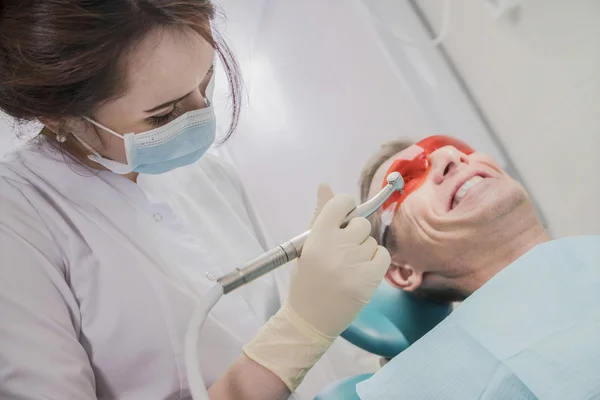 Concepto de cuidado dental inspección estomatológica. el paciente se acuesta en una silla en odontología delante de él una mano con taladro — Foto de Stock