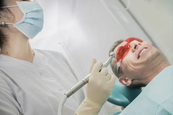 Concepto de cuidado dental inspección estomatológica. el paciente se acuesta en una silla en odontología delante de él una mano con taladro — Foto de Stock