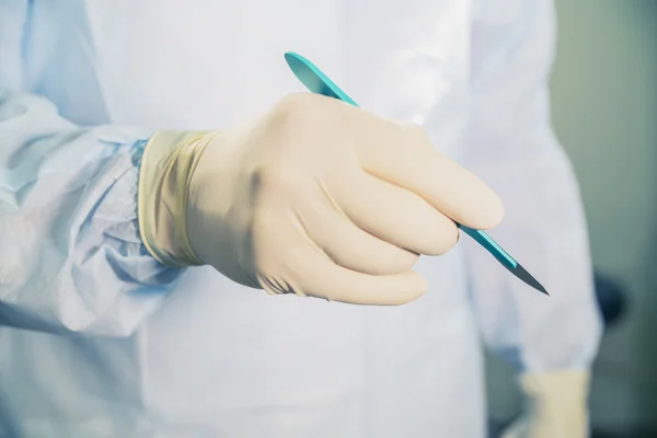 Primer plano de un bisturí en la mano en el fondo de la sala de operaciones — Foto de Stock