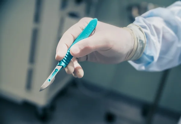 Primer plano de un bisturí en la mano en el fondo de la sala de operaciones — Foto de Stock