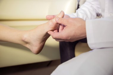 the hands of the doctor examines the foot of a patient clipart