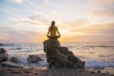 Yoga yapan kadın Lotus pozisyonunda yoga ve meditasyon yapıyor. Akşam okyanusunda açık havada