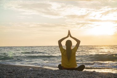 Yoga yapan kadın Lotus pozisyonunda yoga ve meditasyon yapıyor. Akşam okyanusunda açık havada
