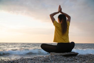 Yoga yapan kadın Lotus pozisyonunda yoga ve meditasyon yapıyor. Akşam okyanusunda açık havada
