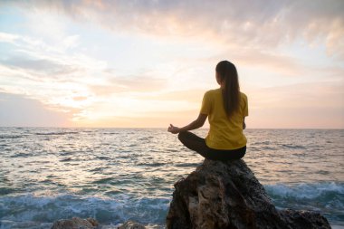 Yoga yapan kadın Lotus pozisyonunda yoga ve meditasyon yapıyor. Akşam okyanusunda açık havada