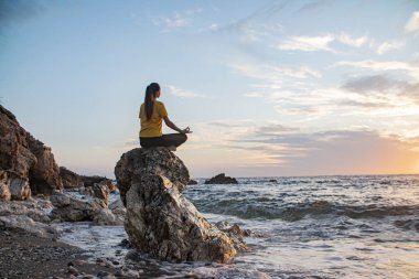 Yoga yapan kadın Lotus pozisyonunda yoga ve meditasyon yapıyor. Akşam okyanusunda açık havada
