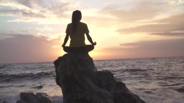 Yoga yapan kadın Lotus pozisyonunda yoga ve meditasyon yapıyor. Akşam okyanusunda açık havada