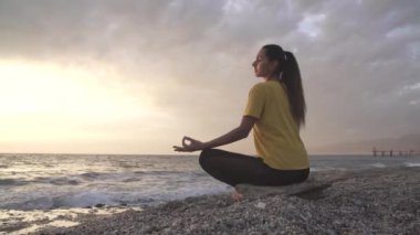 Yoga yapan kadın Lotus pozisyonunda yoga ve meditasyon yapıyor. Akşam okyanusunda açık havada