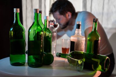 Alkol ve alkolik şişelerinin arkasında içki içen isimsiz bir alkoliğin silüeti.