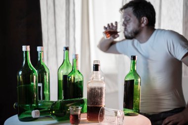 Alkol ve alkolik şişelerinin arkasında içki içen isimsiz bir alkoliğin silüeti.