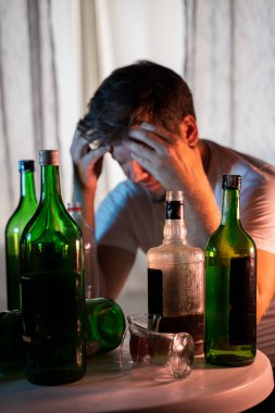 Alkol ve alkolik şişelerinin arkasında içki içen isimsiz bir alkoliğin silüeti.