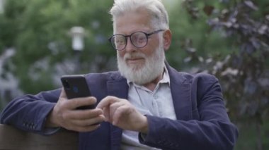 Yaşlı, emekli bir adam telefonda çalışıyor. Sokakta oturuyor.