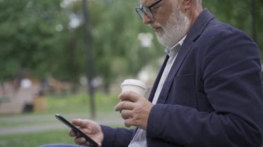 Yaşlı, emekli bir adam telefonda çalışıyor. Sokakta oturuyor.