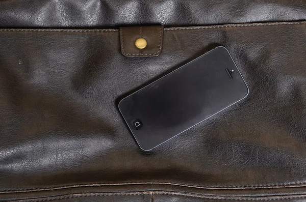 Mobiltelefon liggande på en läderväska Stockbild