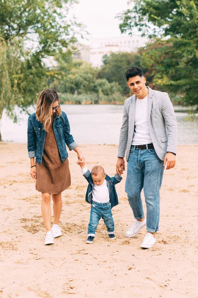 A cute photo of family holding their hands and walking near a lake on sand — Stock Photo, Image