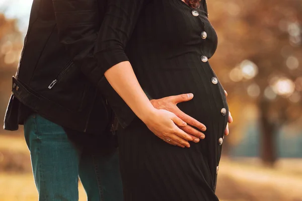 Uma foto de perto de uma mulher grávida e seu marido abraçando sua barriga das costas no parque — Fotografia de Stock