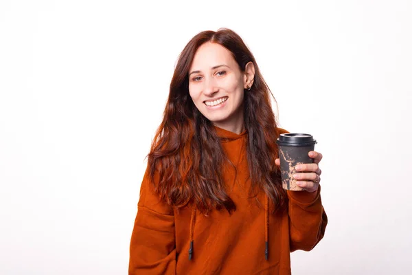 Joven mujer alegre está sonriendo a la cámara y sosteniendo una taza con bebida caliente en ella — Foto de Stock