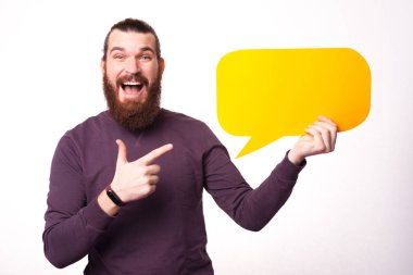 Heyecanlı sakallı ve genç bir adam elinde bir konuşma balonu tutuyor ve ağzı açık kameraya bakıyor.
