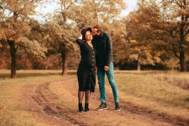 Parkta genç bir ailenin güzel bir fotoğrafı. Kocası hamile karısını yanaktan öpüyor.