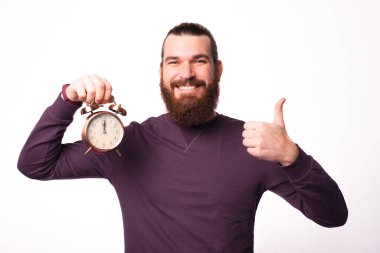 Sakallı genç bir adamın saat tutarken ve başparmağını kaldırırken fotoğrafı.