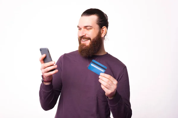 Foto de un hombre barbudo mirando en su teléfono y sostiene una tarjeta de crédito — Foto de Stock