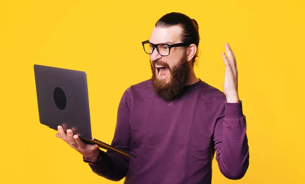 一个戴眼镜的留着胡子的年轻人拿着一台计算机，对着它大叫 — 图库照片
