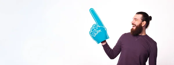 Zdjęcie wesołego młodego brodatego mężczyzny trzymającego rękawicę wentylatora wskazującą na wolną przestrzeń i patrzącego na nią. — Zdjęcie stockowe
