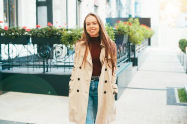 Kameraya gülümseyen kadın sonbahar mevsiminde paltoyla yürüyor.