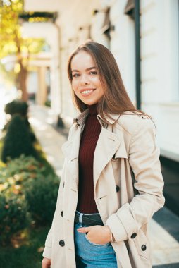 Paltoyla yürüyen bir kadın kameraya bakıp gülümsüyor.